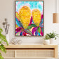 A vibrant abstract floral art print featuring shades of yellow, magenta, and blue displayed on a table with decorative items and a wall lamp in the background.