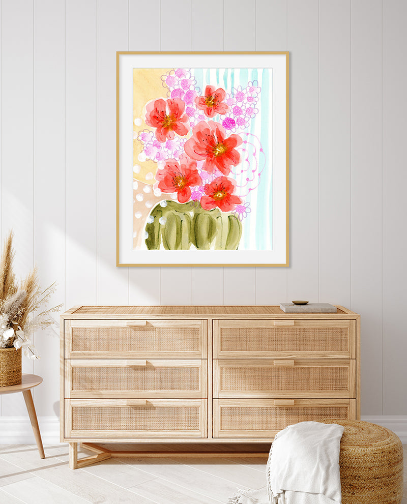 A framed painting titled 'Flowering Hearts' with pink and coral flowers against a light background, displayed above a wooden cabinet.