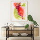 A framed abstract painting with predominantly red and green colors, displayed above a console table in a room with various decorative items.