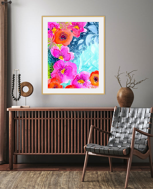 A vibrant abstract floral art print with fiery pinks, radiant oranges, and deep crimsons, titled 'Joyful Garden', displayed in a room setting with a wooden console table and a modern armchair.