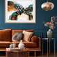 A framed abstract artwork with flowing green, brown, and orange elements displayed on a wall above a brown sofa with decorative pillows, a white vase, and a wooden coffee table in a room with a dark blue wall and a hanging light.